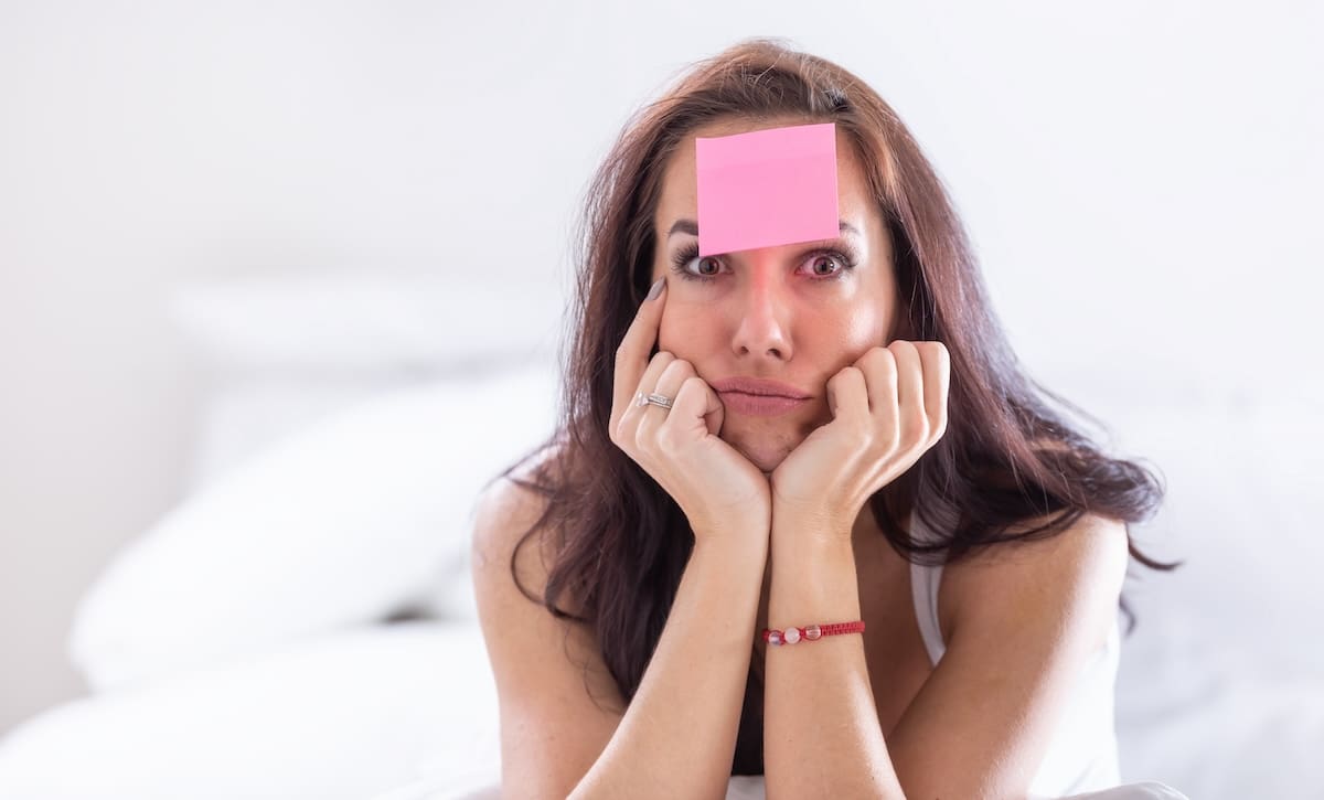 A woman suffering from brain fog puts a post-it note on her forehead to remember